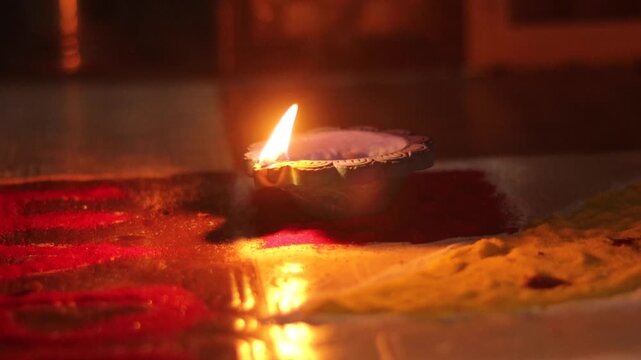 Traditional Indian Clay Diya Lamp Burning with Flame Placed on Colorful Rangoli Powder Art Design for Happy Diwali Festival Celebration Close Up Glowing Earthen Oil Lamp Wick Lit on Vibrant Decorative