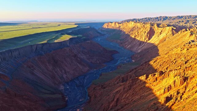 Aerial view of a winding braided river flowing through a deep rocky canyon at sunset in Anjihai Grand Canyon, Xinjiang, China
