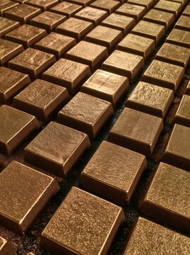 Gold bars arranged in orderly rows on a dark textured surface, featuring a sandblasted finish for financial backgrounds and commodity designs