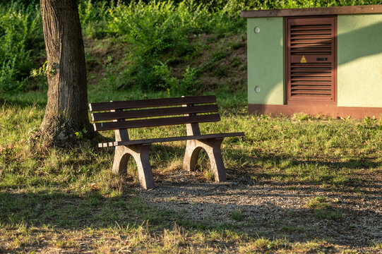 H&ouml;lzerne Sitzbank mit Betonf&uuml;&szlig;en im Seitenlicht der tiefstehenden Sonne vor l&auml;ndlichem Trafoh&auml;uschen in Neckartenzlingen