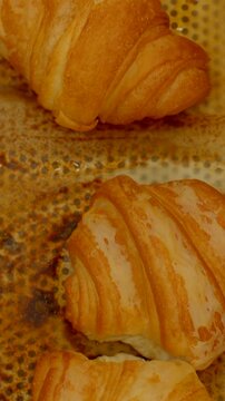close-up vertical shot of multiple golden-brown croissants resting on perforated metal tray showing flaky laminated layers, glossy butter patches, and small oil