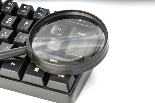 Close-up shot of a magnifying glass placed over a black mechanical keyboard, emphasizing the Enter key and surrounding keys like Shift and bracket symbols
