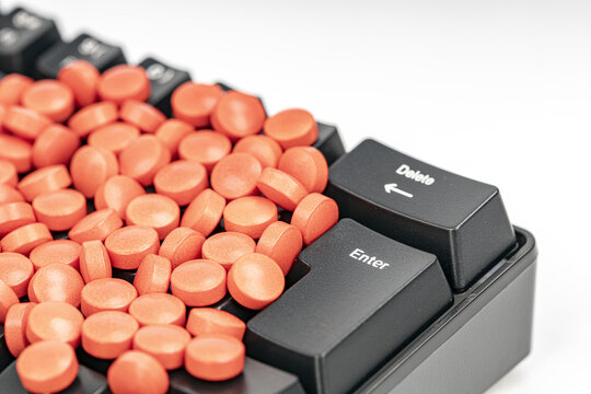 Close-up of numerous orange pills scattered over a black computer keyboard next to the enter and delete keys, representing health, medication and online pharmacy risks