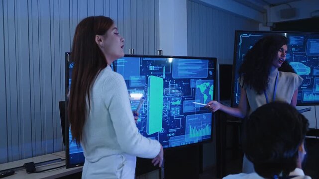 Diverse engineering team reviewing interactive digital display during software design presentation while female specialist points at screen interface in office workstation area