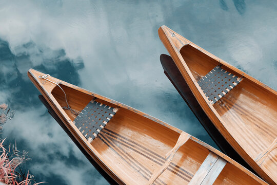 Wooden canoes resting on tranquil lake water, reflecting the sky. Representing nature, peace, and outdoor adventure