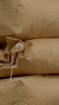 vertical close-up of stacked brown kraft paper sacks with twisted white twine hanging in foreground, showing folded ends, seams, tape patches, and crumpled paper