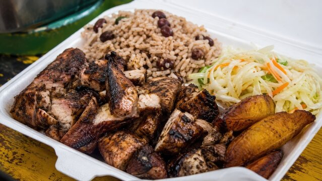 Takeout container with jerk chicken, rice and peas, fried plantains and cabbage slaw