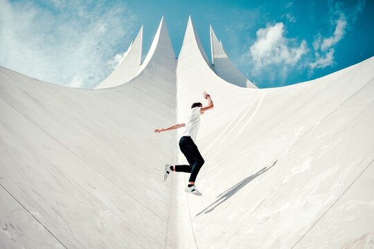 action shot of man running and jumping parkour style across a white roof with a blue sky background