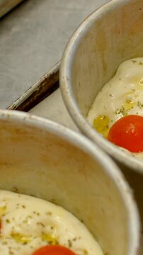 vertical close-up of ceramic ramekin filled with fully melted white cheese topped with whole cherry tomatoes, olive oil pools, and dried herb sprinkles, interior