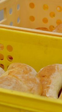 close view of golden bread loaves being placed into stacked yellow perforated bakery crates, highlighting crust texture and warm indoor light reflections soft bread