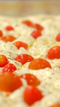 low-angle close-up of focaccia or flatbread showing glossy whole cherry tomatoes nestled in melted white cheese and pillowy dimpled dough, sprinkled with dried dough