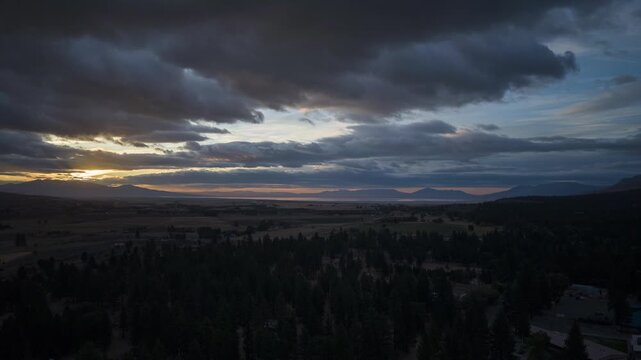 Drone hyperlapse rising above Janesville, California at sunrise as a storm moves in, warm golden light breaking through dramatic storm clouds over the valley.