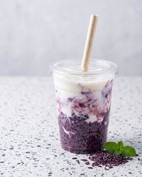 Purple rice and milk smoothie in plastic takeaway cup with paper straw on marble table