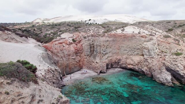 Reveal of Tsigrado Beach in Milos, Greece. Breathtaking turquoise sea and volcanic cliffs with a hidden sandy cove. Exotic Mediterranean travel scene