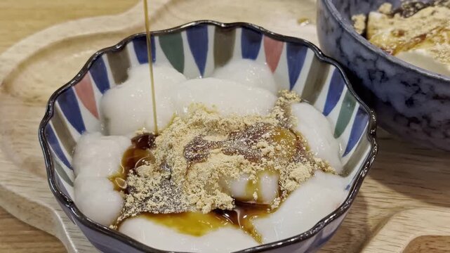 Close-up of soft white shiratama dango topped with fragrant kinako powder and sweet syrup, served in a decorative ceramic bowl as a traditional Japanese dessert.