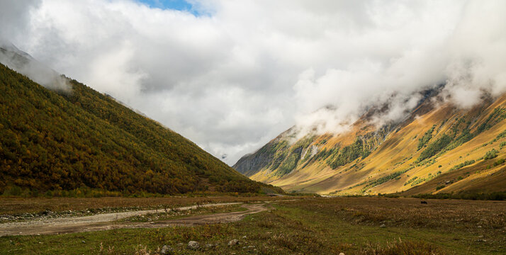 Landscape photograph of mountain valley with dirt road and low clouds in Svaneti Georgia.