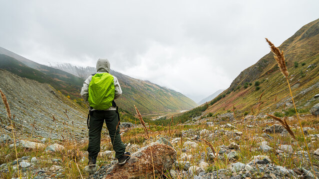 Hiker with green backpack standing looking at autumn mountain valley near Shkhara glacier in Georgia.