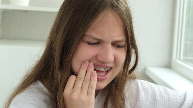 Teenage girl with braces on teeth touching her cheek with hand because of toothache. Concept of dental pain