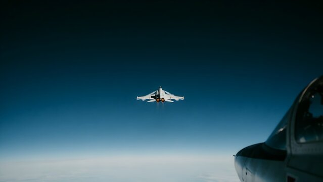 Military fighter jet flying high in clear blue sky with aircraft carrier nearby