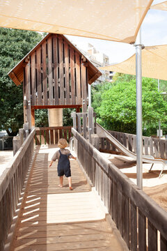 Kid enjoying and running in wooden playground structure with metal slide under large shade sails in a public urban park. Outdoor recreational area for children with safe play equipment