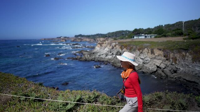 Senior woman hikes along the headlands enjoying the flowers and ocean views in Mendocino Coast Botanical Gardens.