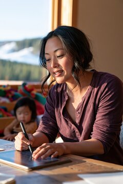 Woman sketching on tablet with stylus near window in cozy workspace for creative design and digital art background