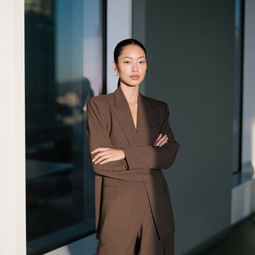 Confident woman in brown tailored suit standing by window for corporate profile and professional branding banner