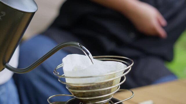 Making pour-over coffee with a gooseneck kettle outdoors, this slow-brewing method highlights an artisanal approach to a mindful morning ritual while camping in nature.