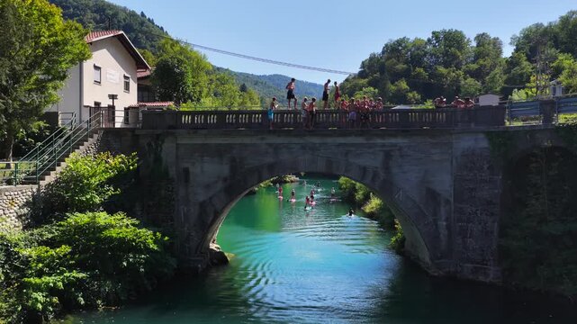 Aerial view of Most na Soci with the Soca River, Santa Lucia, Slovenia. Canoes, SUPs, and swimmers in the water.