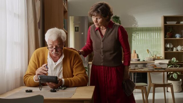 Senior Caucasian man repairing vintage electronics while senior woman watches supportively at home. Video suitable for retirement lifestyle advertising and senior living promotions
