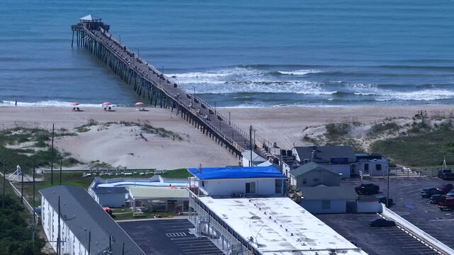 Atlantic Beach, NC Fishing pier with gentle breaking ocean waves and people on beach on sunny day