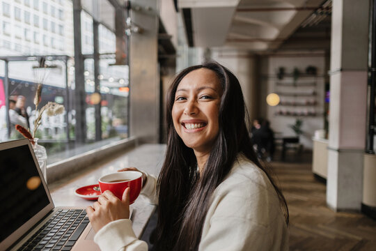 Asian woman smiling enjoying coffee working on laptop in cafe