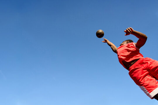 Man Jumps to Catch a Football Under a Clear Blue Sky
