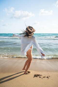 Woman Twirling on the Beach Near the Water Under a Clear Sky