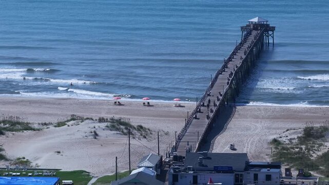 Atlantic Beach, NC Fishing pier with gentle breaking ocean waves and people on beach on sunny day