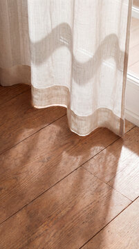 Sheer curtain casts soft shadow patterns across warm wooden floorboards indoors