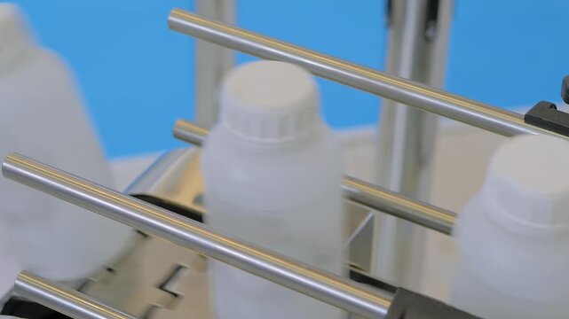 Conveyor belt of bottle shrink sleeve labeling machine with empty white plastic bottles at packaging trade show, exhibition or factory: close up view, production line, demonstration mode