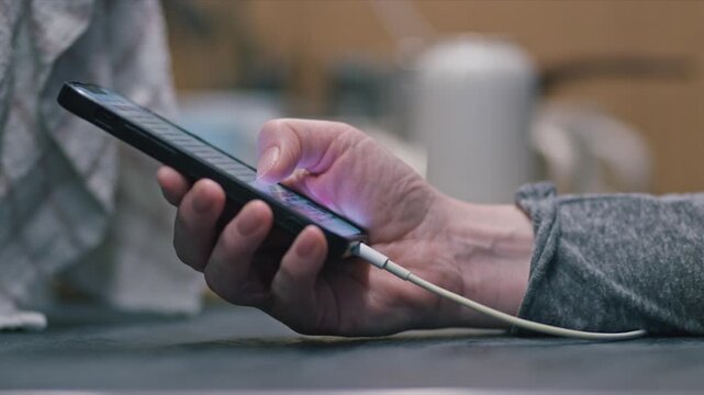 Close-up of female person holding charging smartphone while using touchscreen at home, 4K