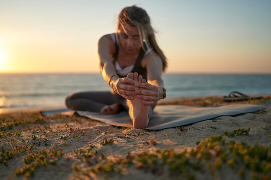 Woman Stretching in Seated Forward Fold Yoga Pose on Beach Mat