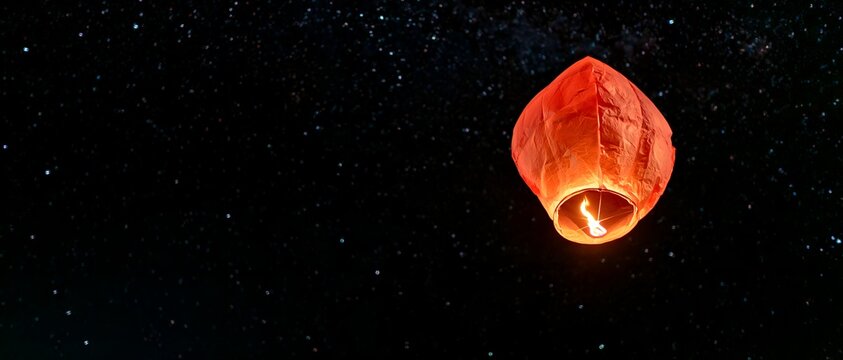 Orange lantern with bright flame rises above stars at night