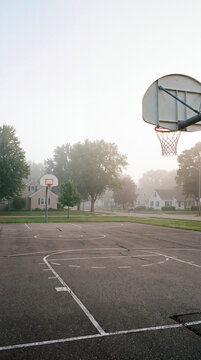 Empty basketball hoop stands in misty neighborhood court during quiet morning