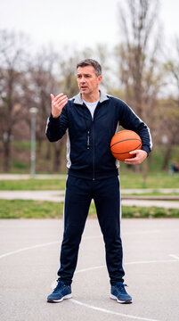 Basketball coach holds ball while giving instructions on outdoor court