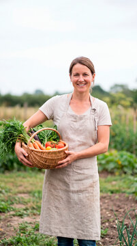 Smiling farmer holds wicker basket filled with fresh harvested vegetables