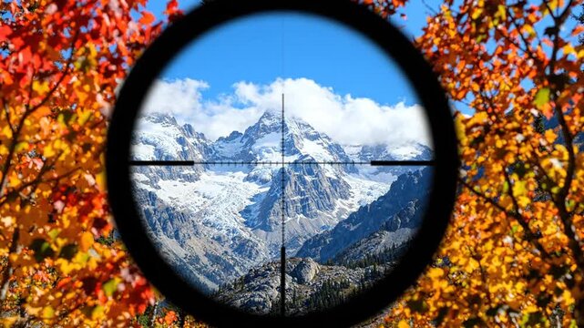 View of snowy mountain peak seen through a rifle scope in autumn forest