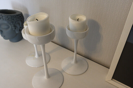 White Blomster candle holders with slender stems and circular bases hold unlit pillar candles. gray Buddha‑head vase adds subtle contrast
