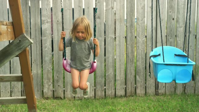 Young boy swinging on a pink swing in a backyard on an overcast summer day