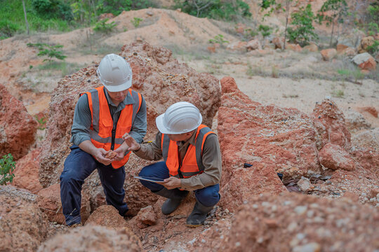 Two male geologists inspect rock and soil samples while reviewing field data on a tablet at an excavation site. Concept of geology, field survey, earth science, and geological investigation.