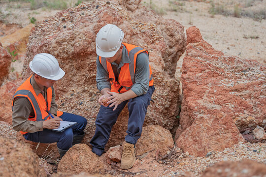 Two male geologists inspect rock and soil samples while reviewing field data on a tablet at an excavation site. Concept of geology, field survey, earth science, and geological investigation.