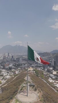Aerial ascending shot of the monumental Mexican flag on Cerro del Obispado with Cerro de la Silla behind, Monterrey, Nuevo Le&oacute;n. Vertical video. D-Log M