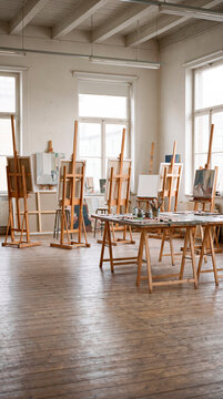 Sunlit art studio displays wooden easels and canvases across open floor
